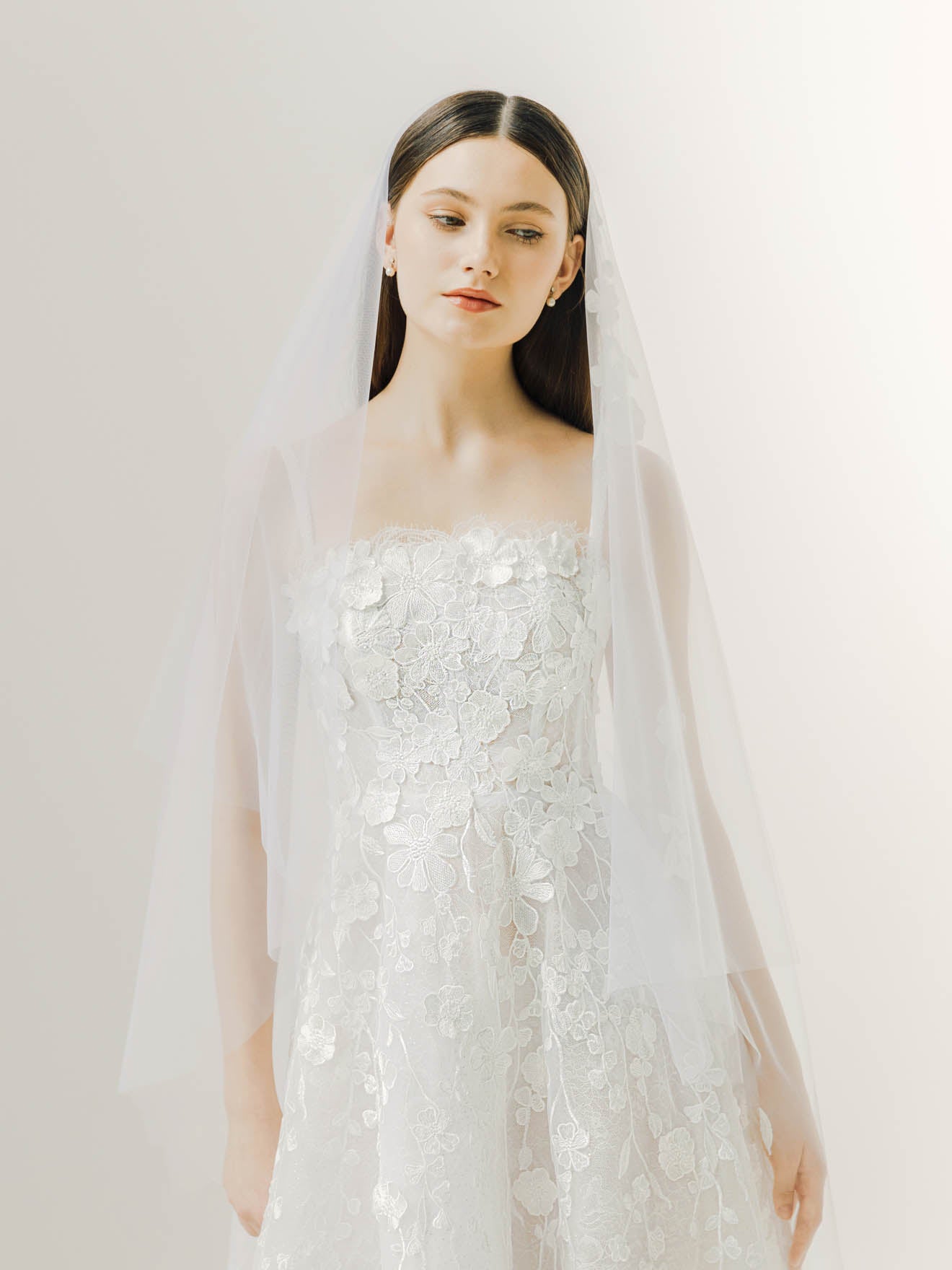 Woman wearing a white wedding dress with a veil against a plain background