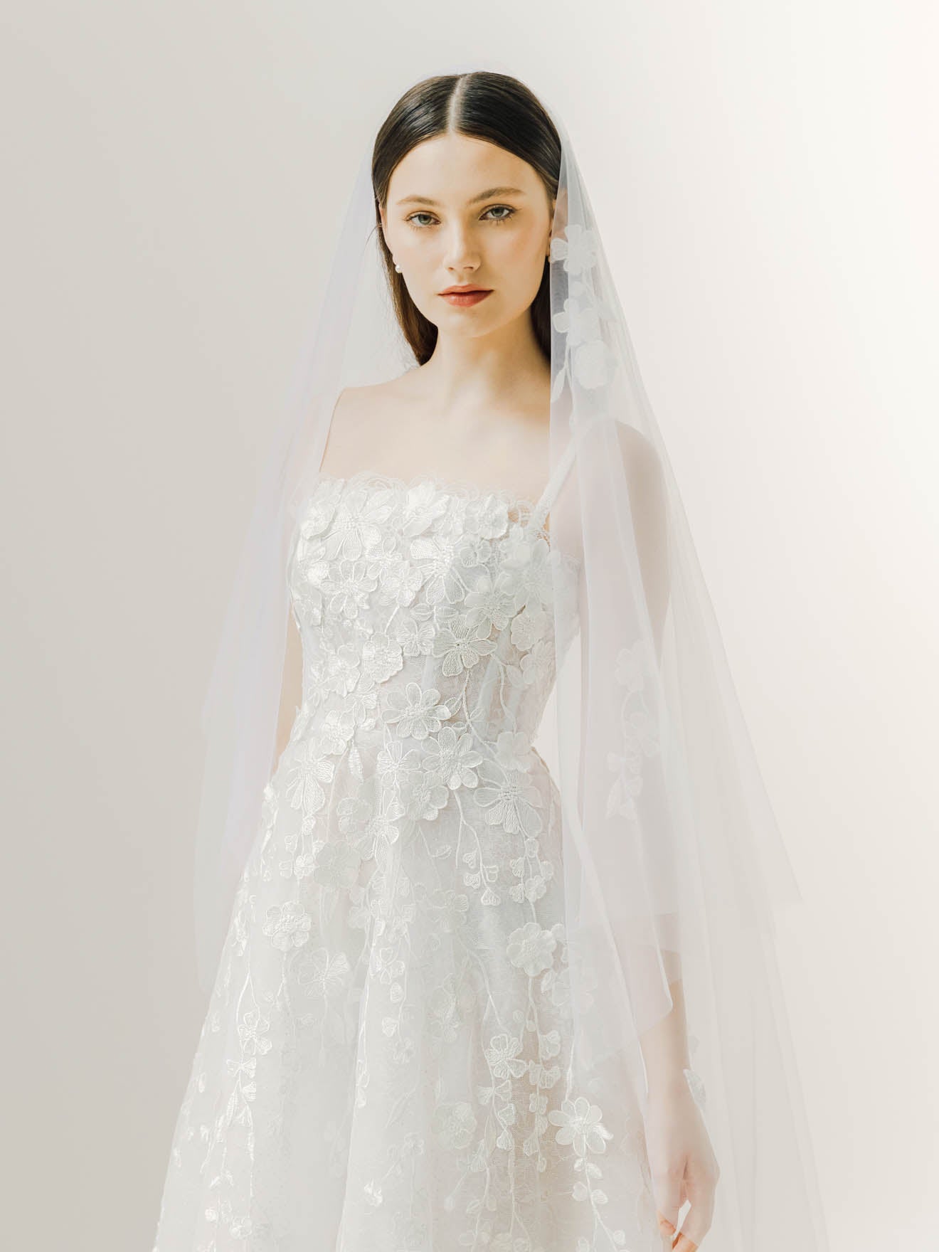 Woman wearing a white wedding dress with a veil against a plain background