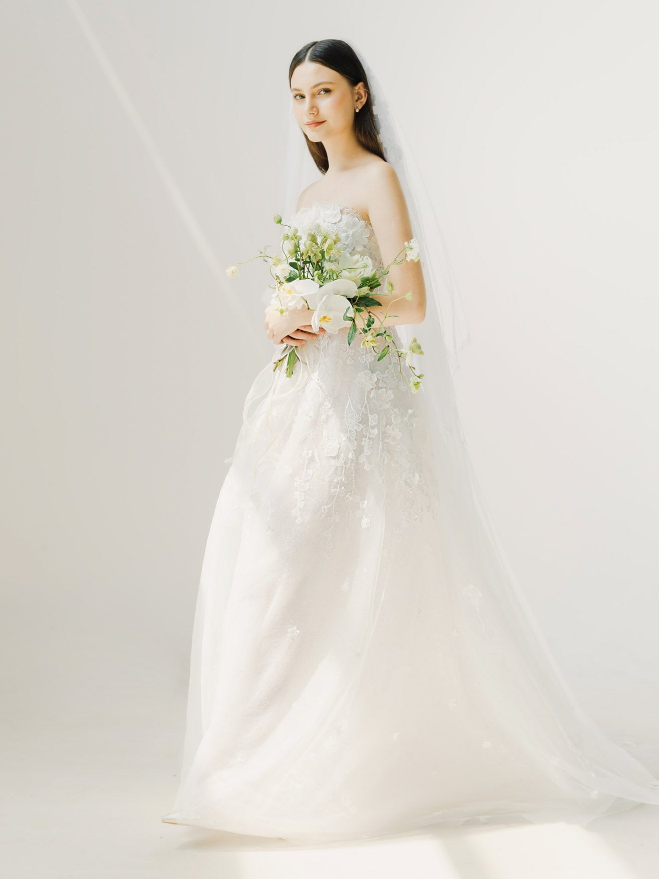 Bride in a white wedding dress holding a bouquet against a plain background