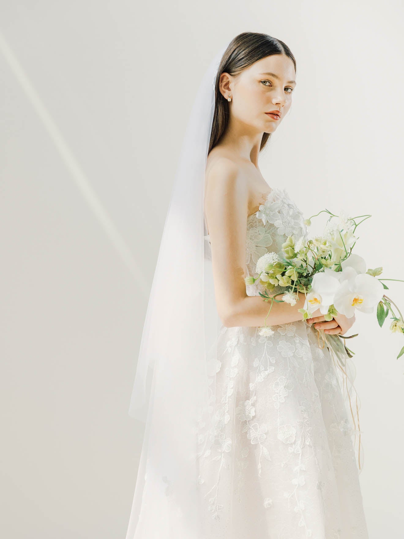Bride in a white wedding dress holding a bouquet against a plain background