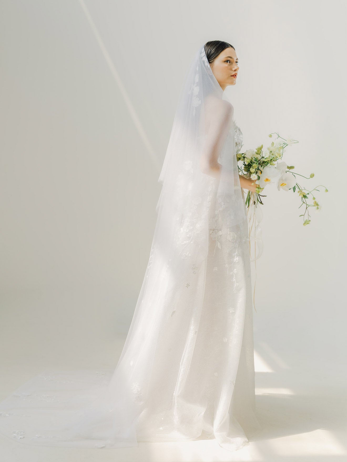 Woman in a white wedding dress holding flowers against a plain background