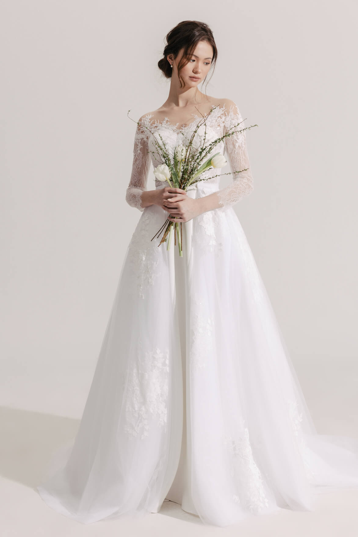 Woman in a white wedding dress holding a bouquet against a plain background