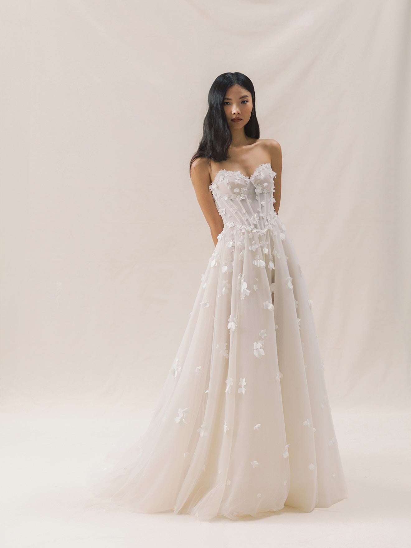 Woman wearing a strapless wedding dress with floral details on a plain background