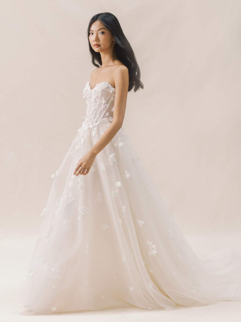 Woman wearing a strapless wedding dress with floral details against a plain background