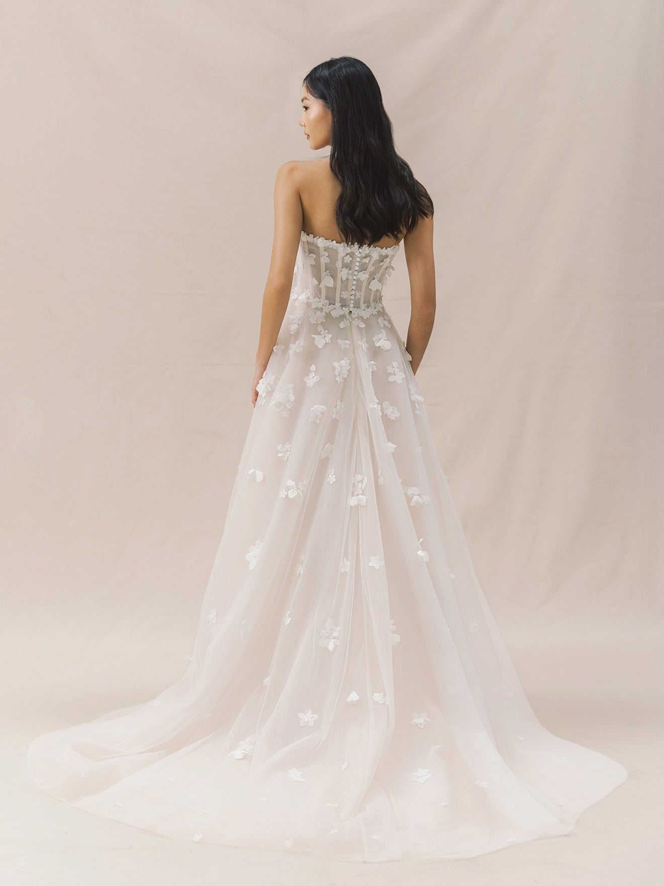 Woman wearing a strapless wedding dress with floral details on a beige background