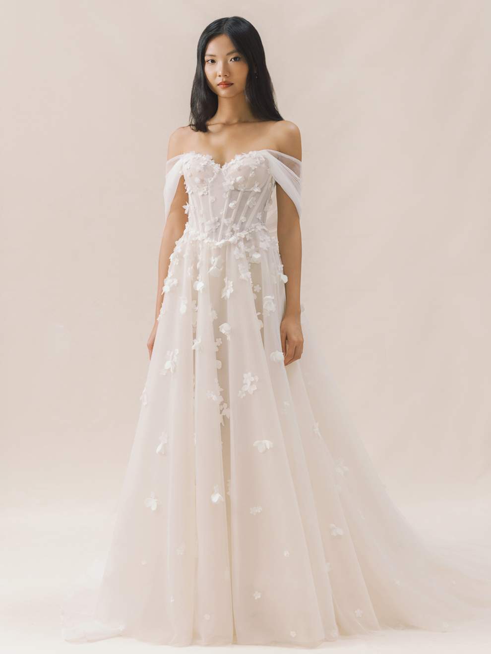 Woman wearing a white floral wedding dress against a plain background