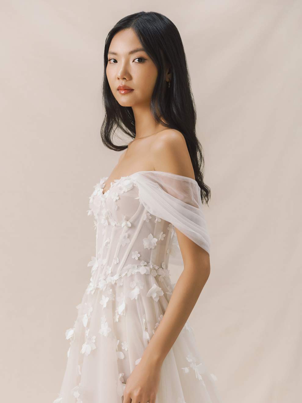 Woman wearing a white off-shoulder dress with floral details against a beige background
