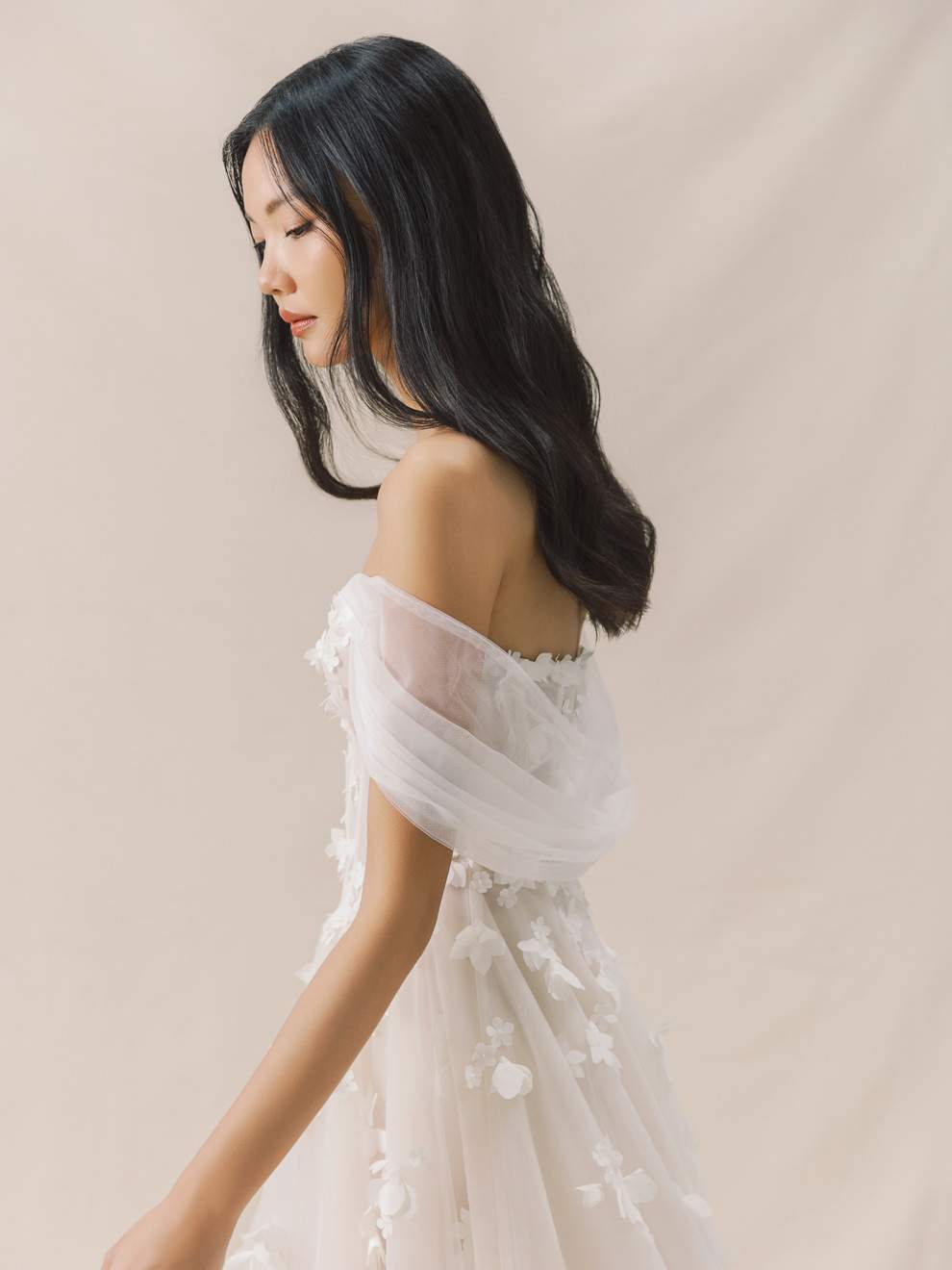 Woman wearing a white off-shoulder dress against a beige background