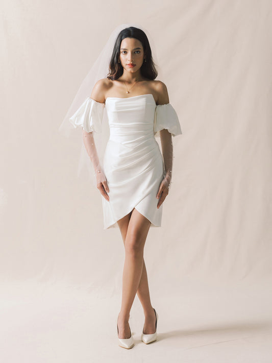 Woman wearing a white off-shoulder dress against a plain background