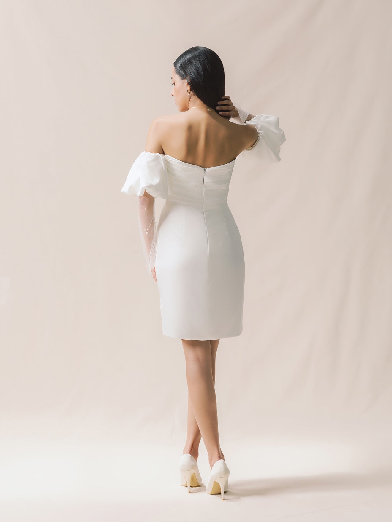Woman wearing a white off-shoulder dress against a beige background