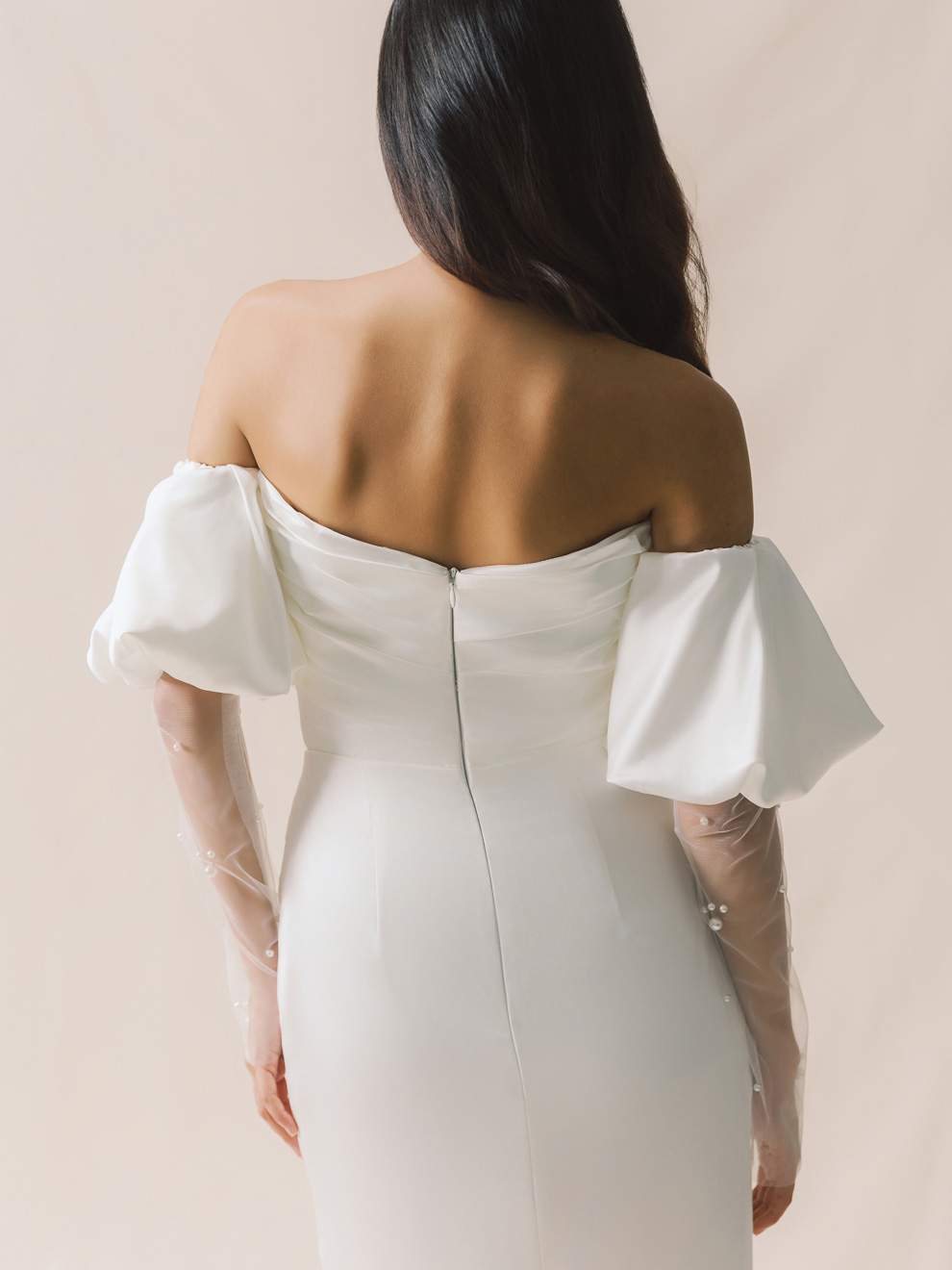 Woman wearing a white off-shoulder dress with ruffled sleeves on a beige background
