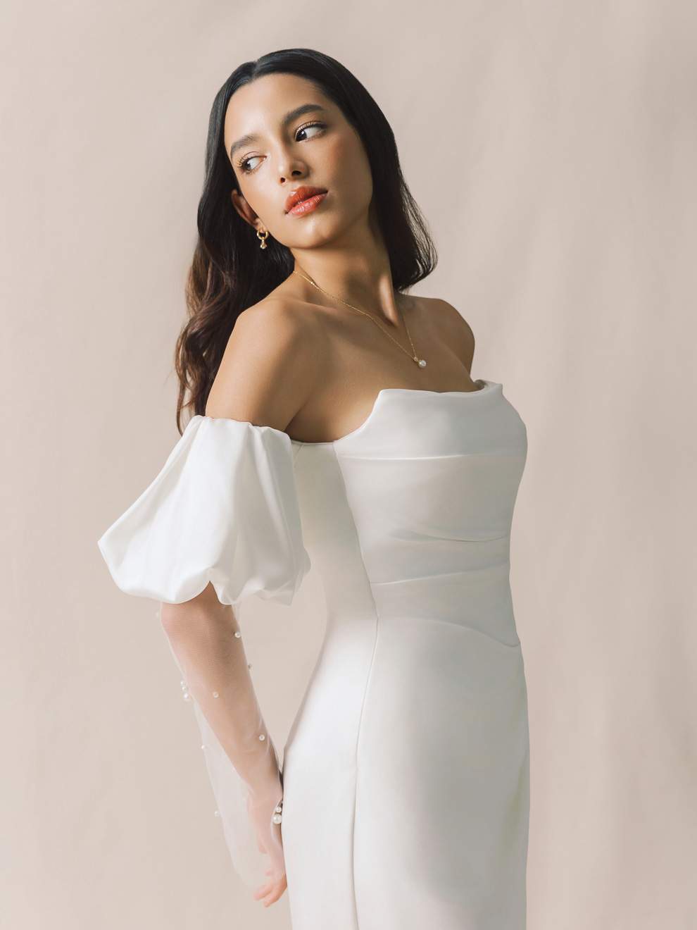 Woman wearing a white off-shoulder dress against a plain background