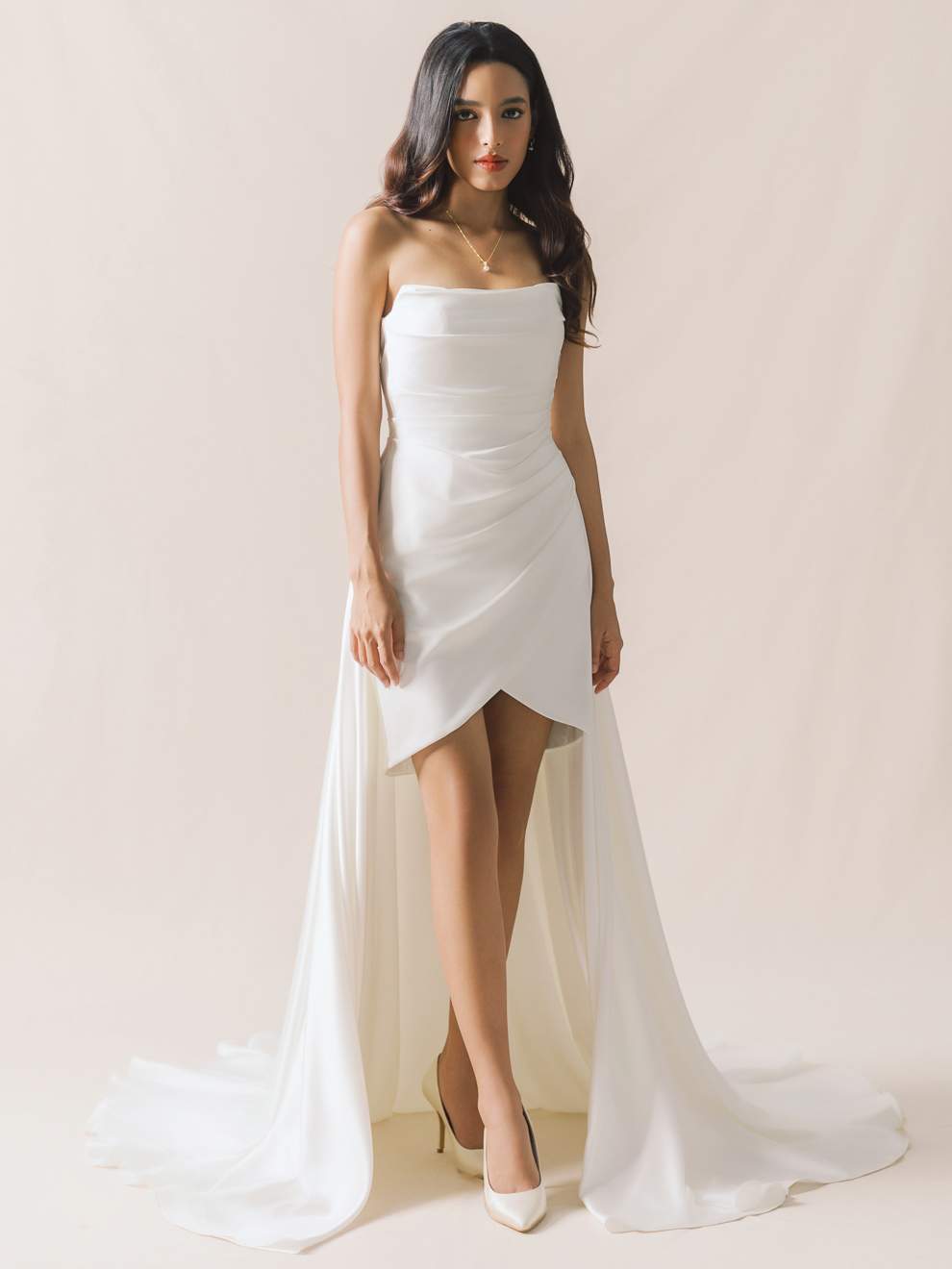 Woman wearing a strapless white gown with a slit on a plain background