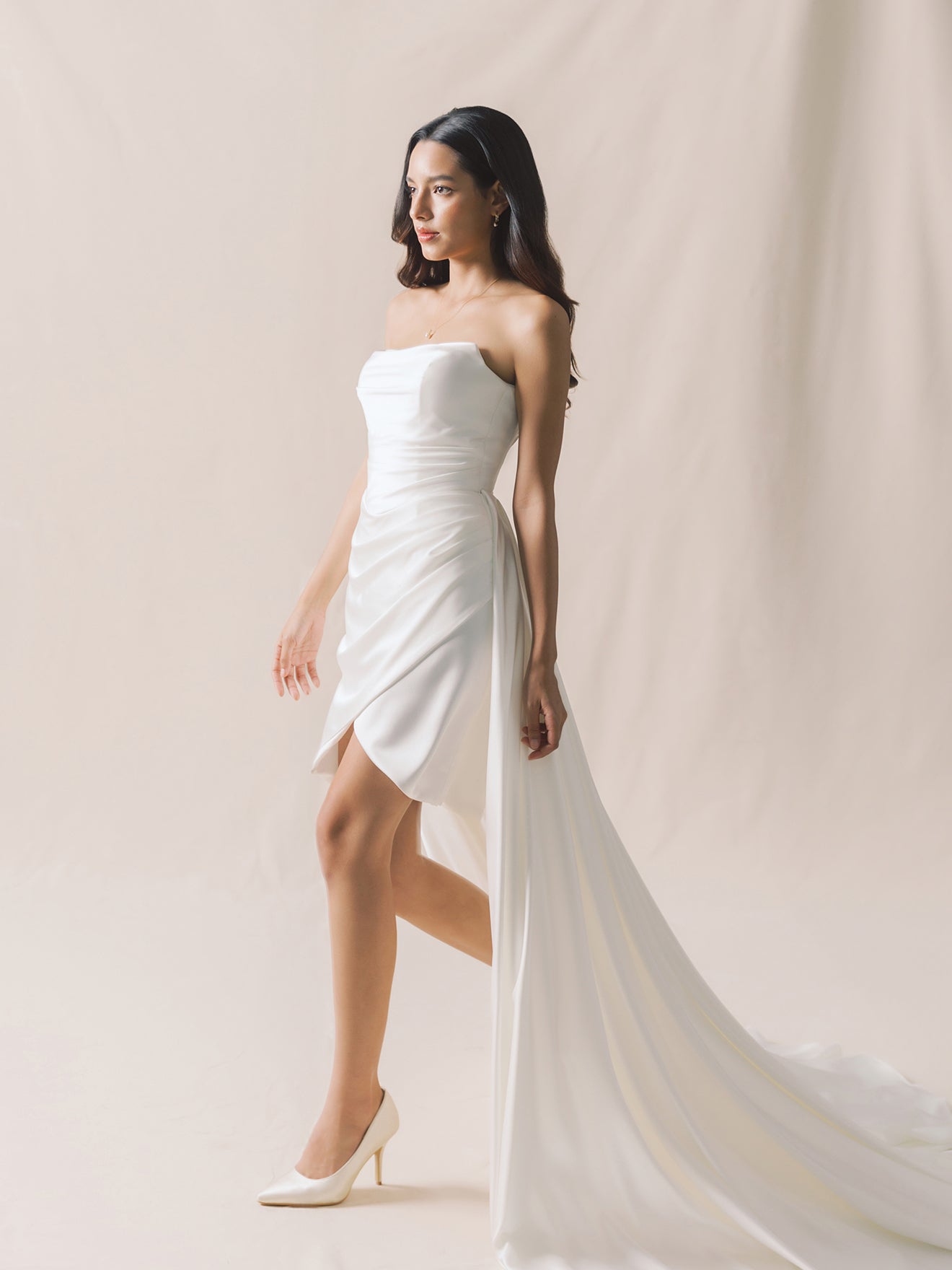Woman wearing a white strapless dress with a flowing train against a beige background