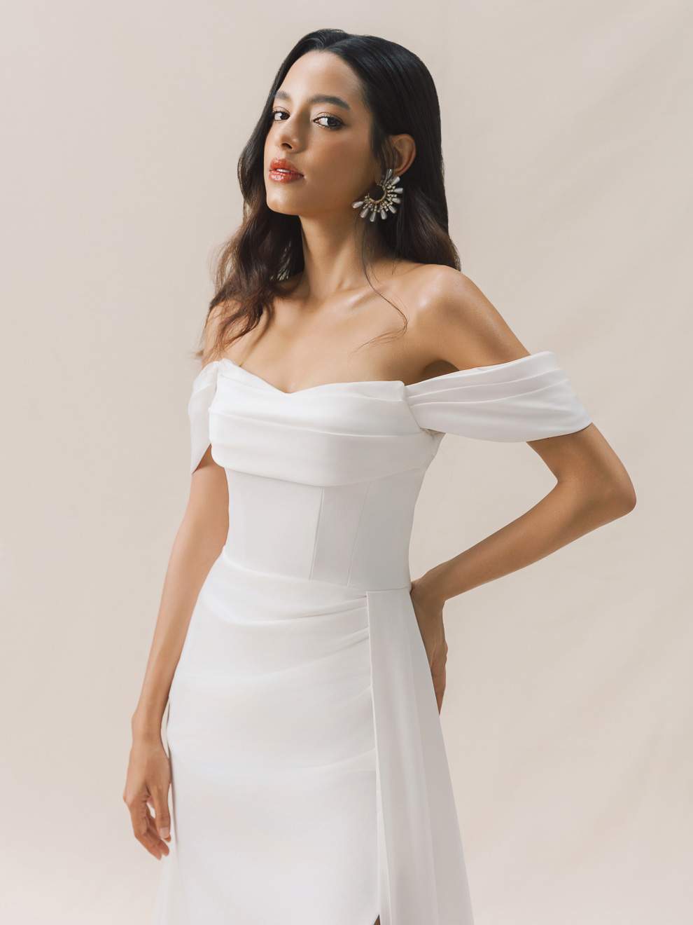 Woman wearing a white off-shoulder dress against a plain background