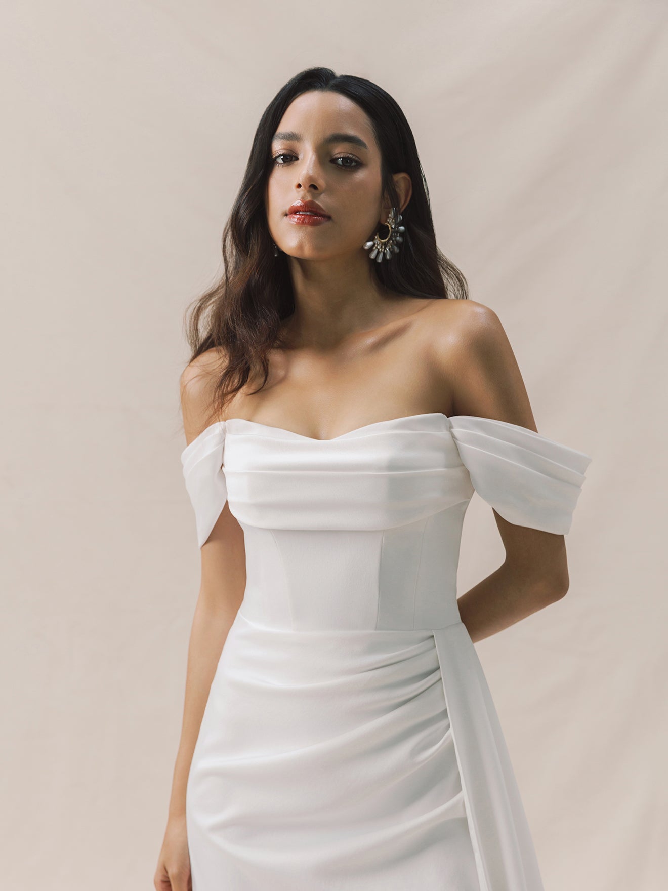 Woman wearing a white off-shoulder dress against a beige background