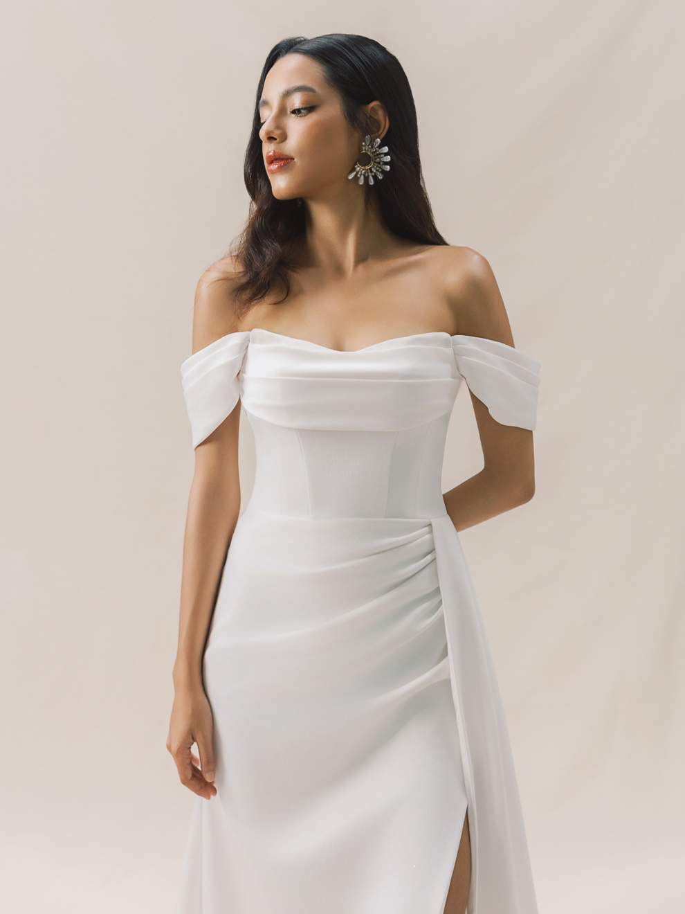 Woman wearing a white off-shoulder dress with a slit on a plain background