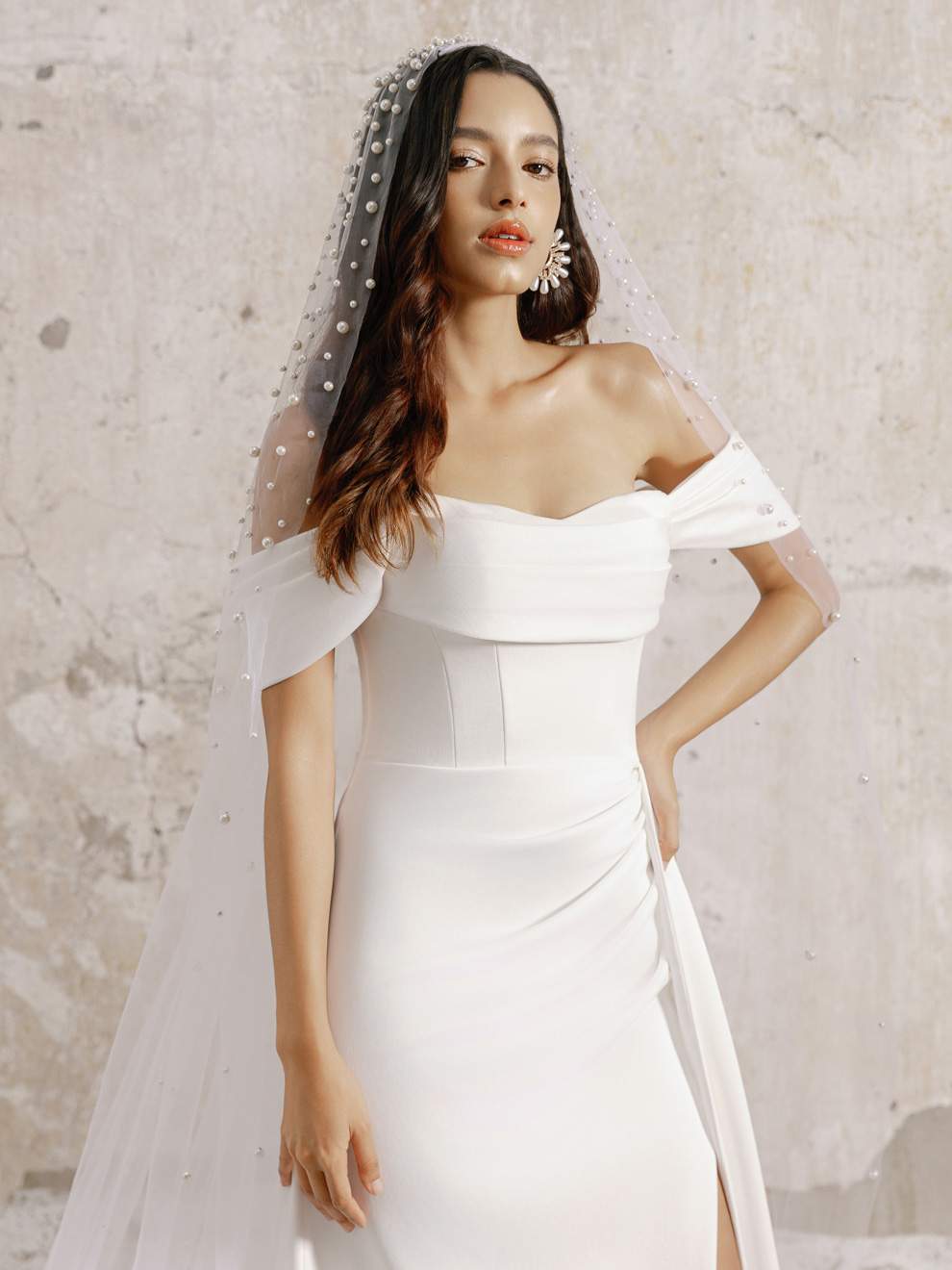 Woman wearing a white off-shoulder wedding dress with a veil against a light background