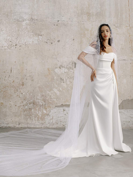 Woman in a white wedding dress with a long train against a textured wall.