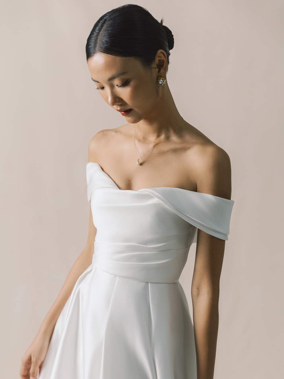 Woman wearing a white off-shoulder dress against a beige background