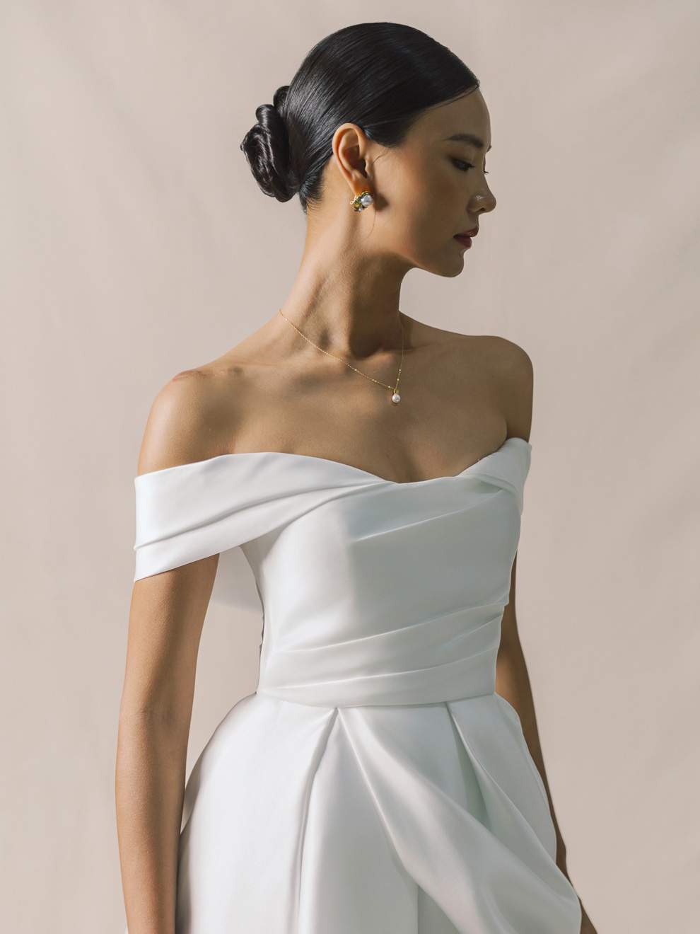 Woman wearing a white off-shoulder dress against a beige background