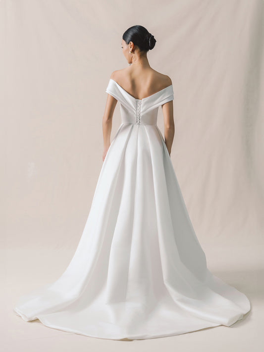 Woman wearing a white off-shoulder wedding dress against a beige background
