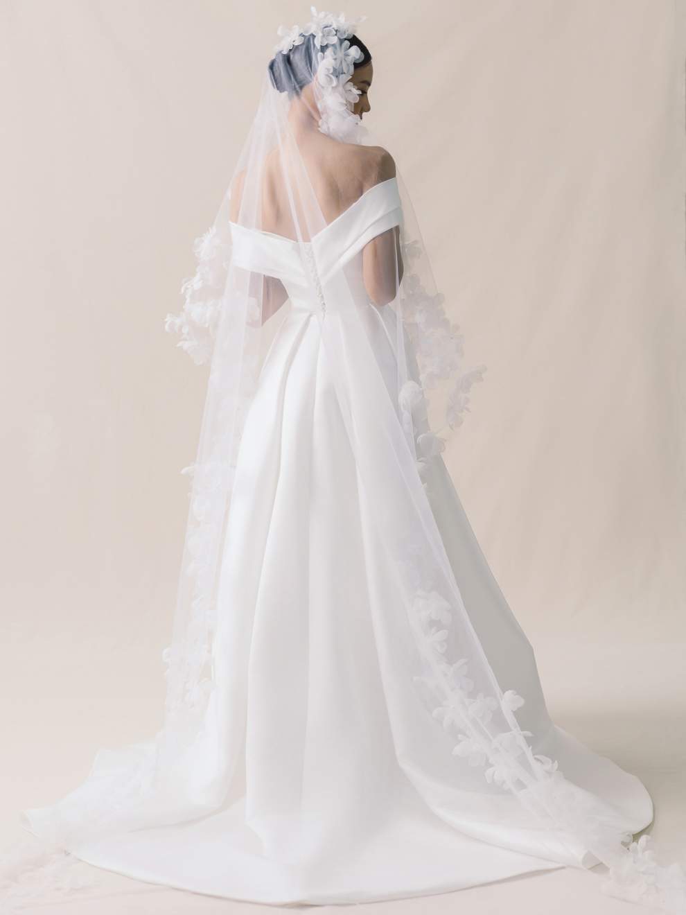 White wedding dress with a long train and floral headpiece on a plain background