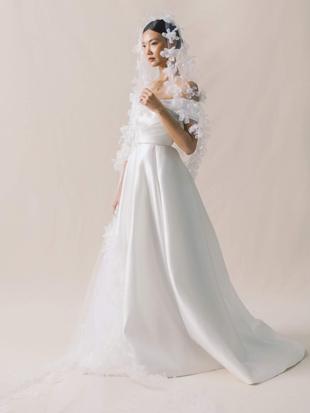 Woman wearing a white wedding dress with a long train and floral headpiece on a plain background
