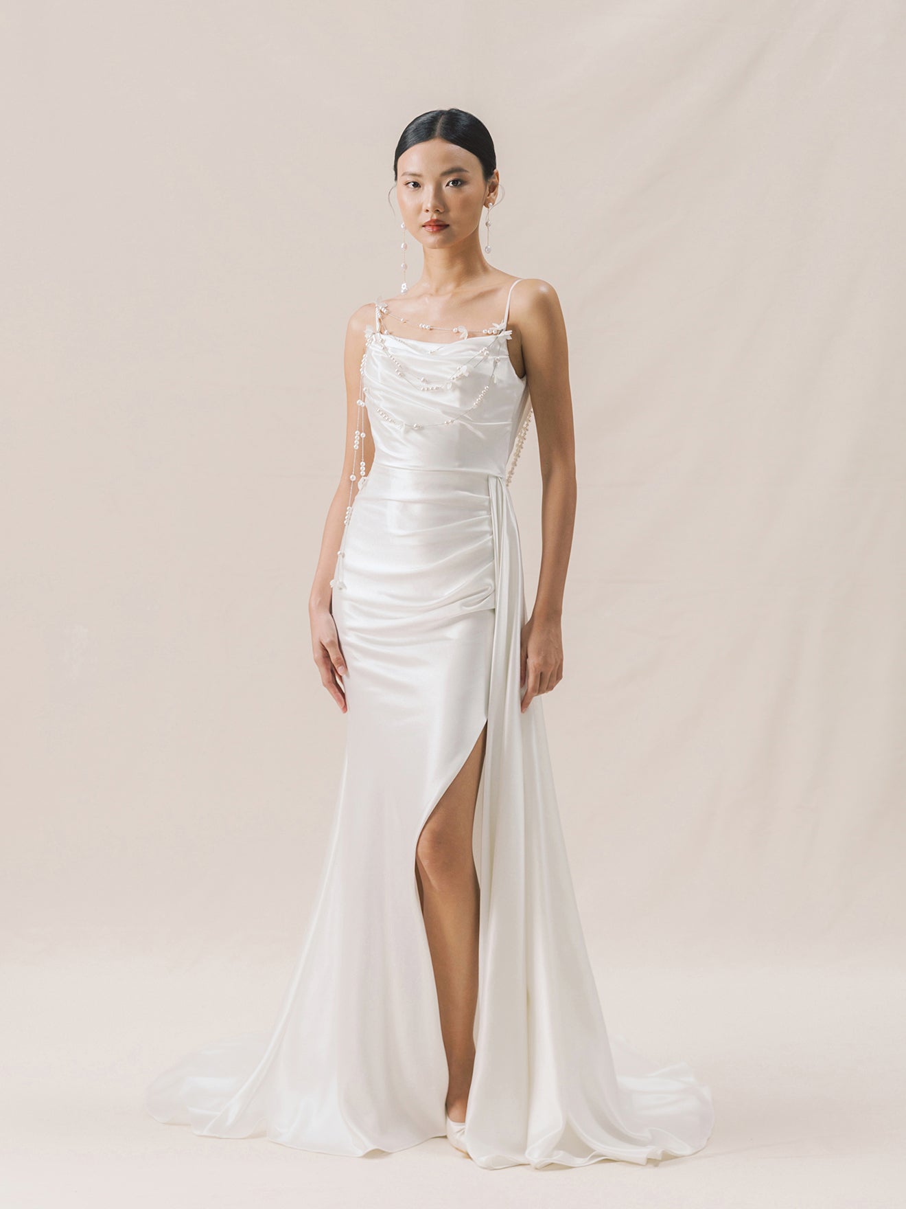 Woman wearing a white wedding dress with a slit on a beige background