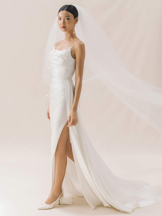 Woman in a white wedding dress with a long train against a plain background