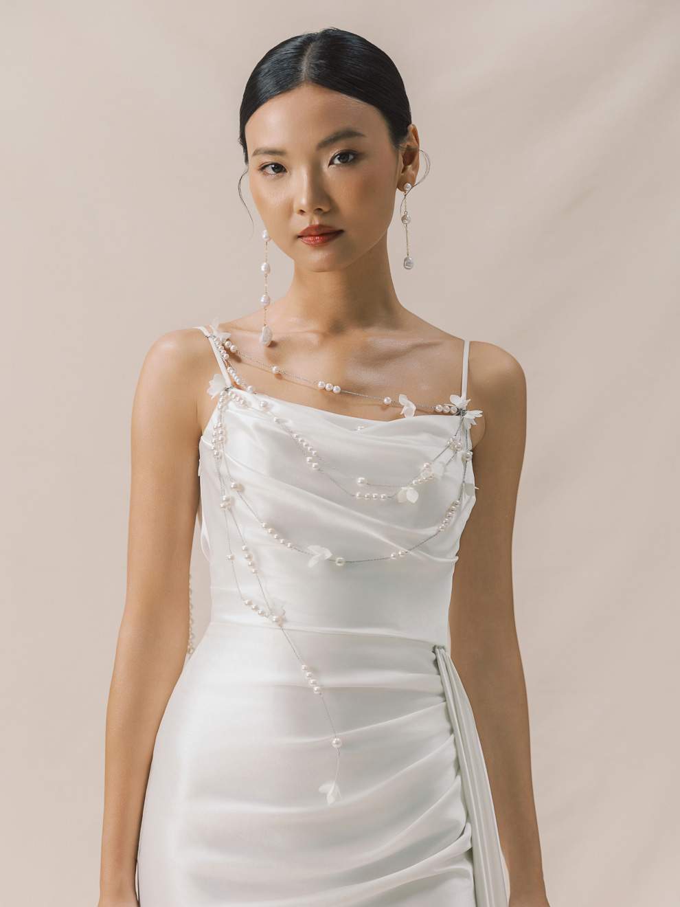 Woman wearing a white dress with floral embellishments against a beige background