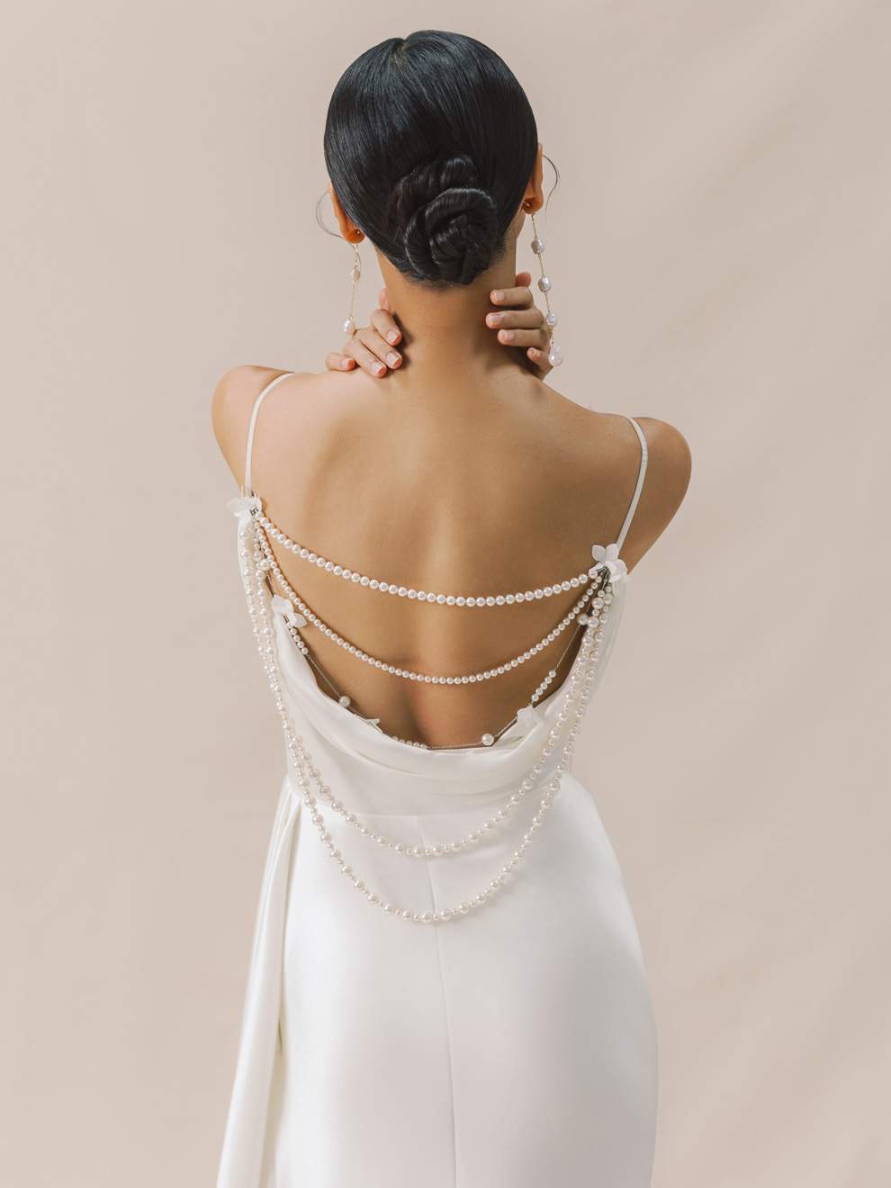 Woman wearing a white dress with pearl straps against a beige background