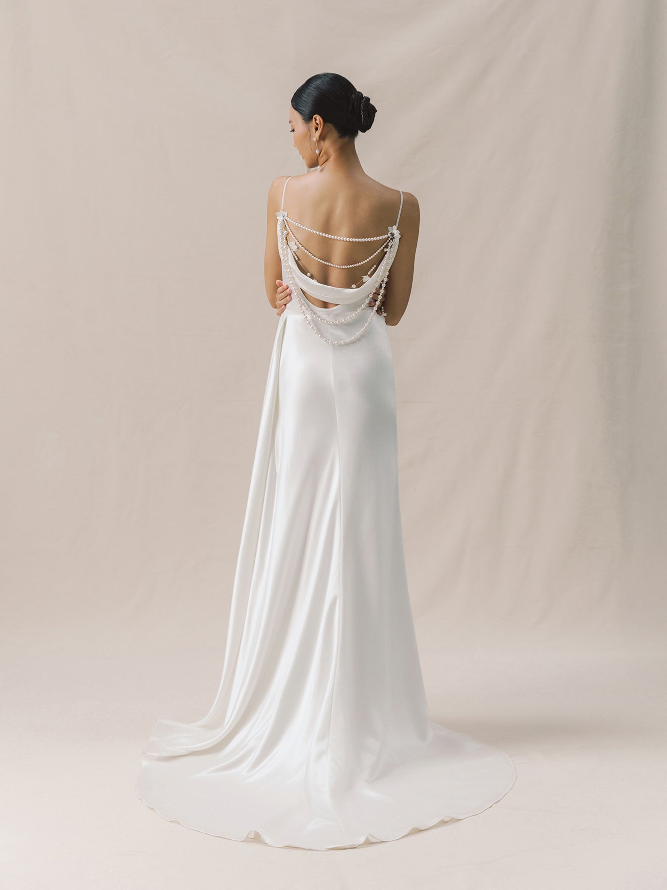 Woman wearing a white wedding dress with an open back against a beige background