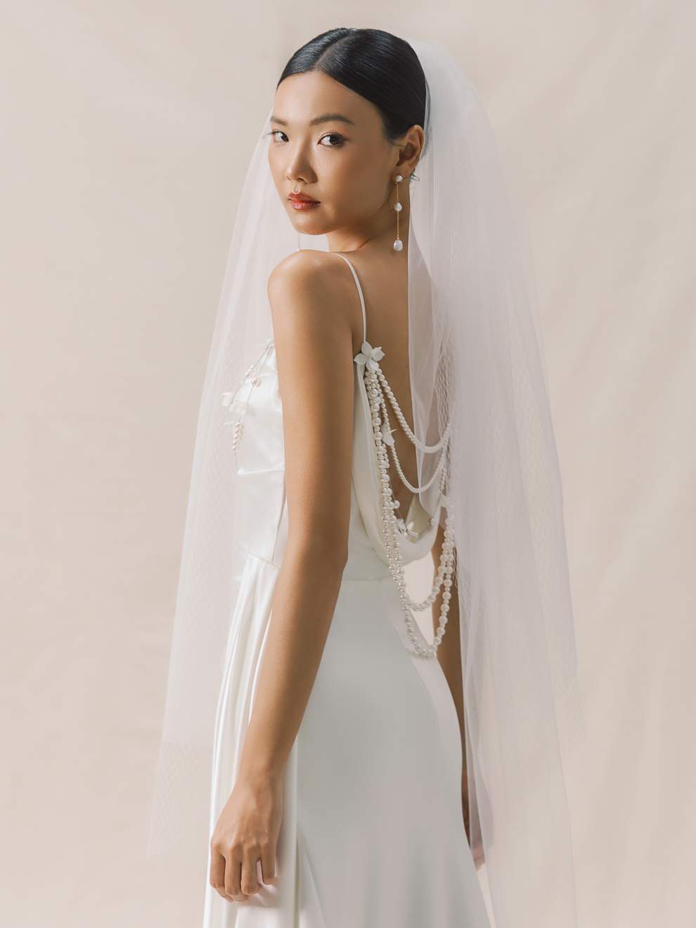 Woman wearing a white wedding dress with a long veil against a plain background