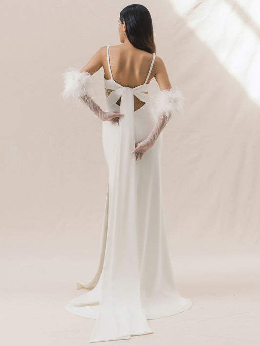 Woman wearing a white wedding dress with feathered sleeves against a beige background