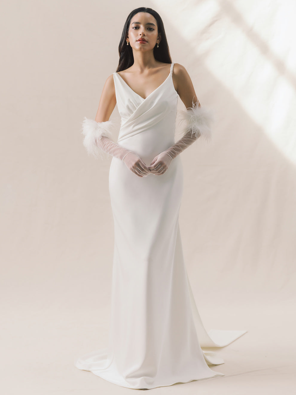 Woman wearing a white wedding dress with sheer gloves against a light background