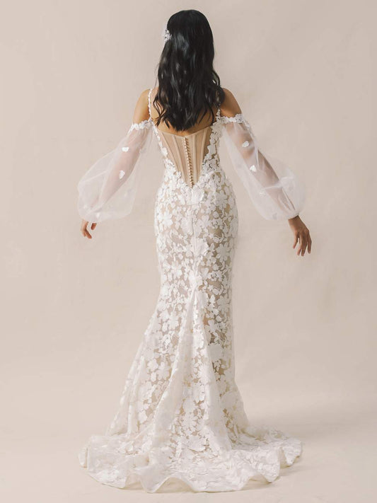 Woman wearing a white lace wedding dress with sheer sleeves on a beige background
