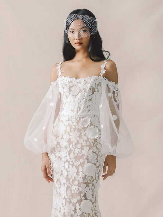 Woman wearing a white floral dress with sheer sleeves against a beige background