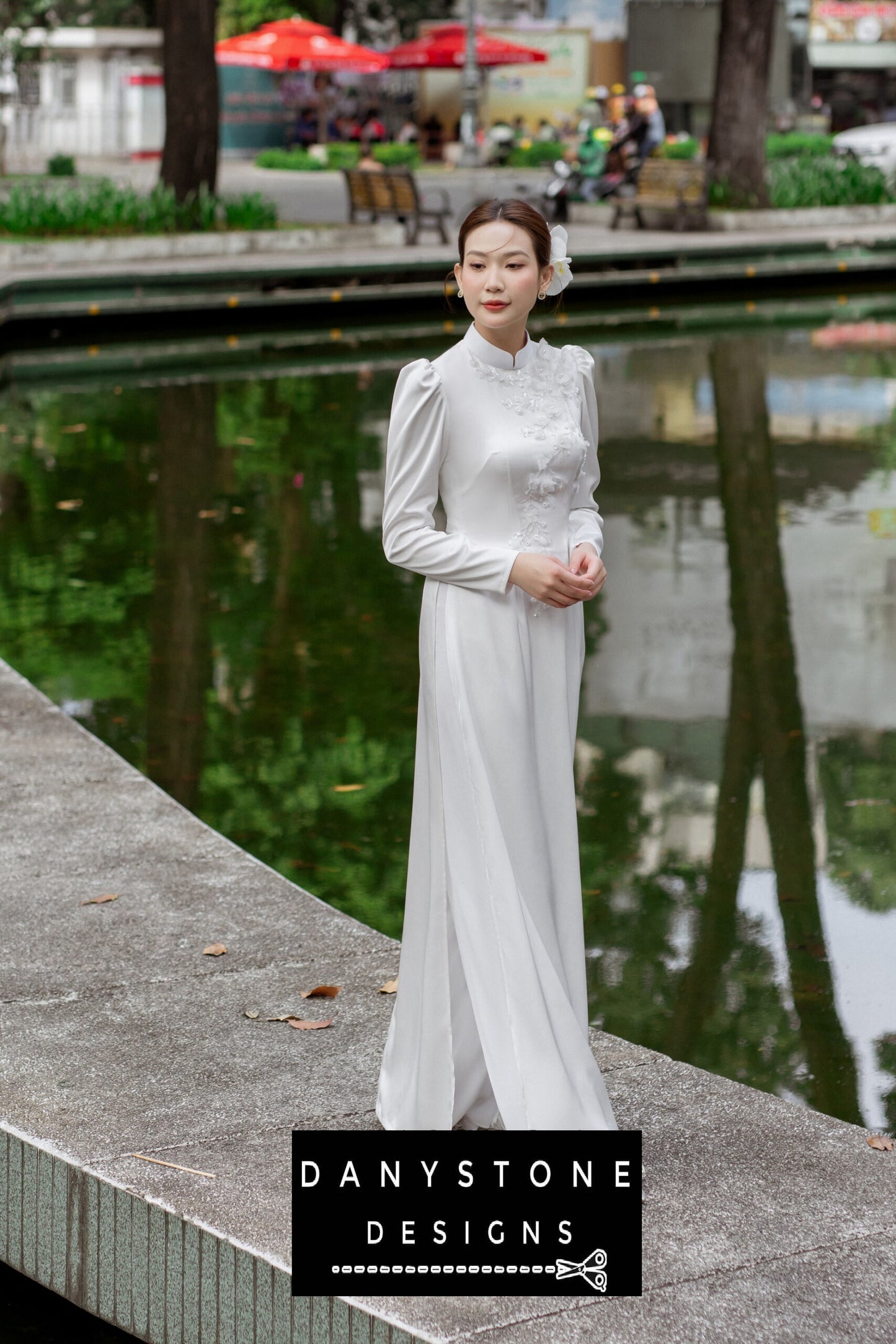 Side view of a woman in a white silk chiffon Áo Dài, showcasing the delicate floral embellishments.