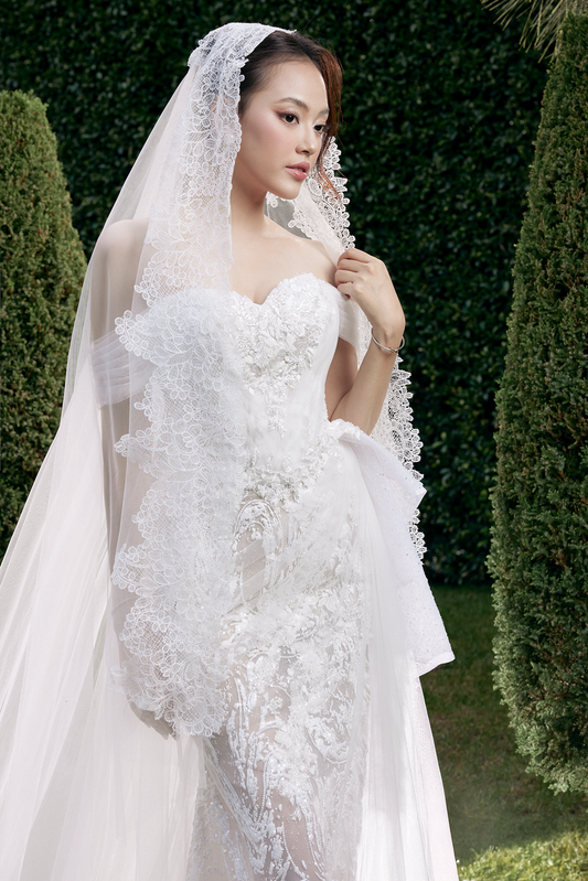 Woman in a white wedding dress with a long veil standing outdoors.