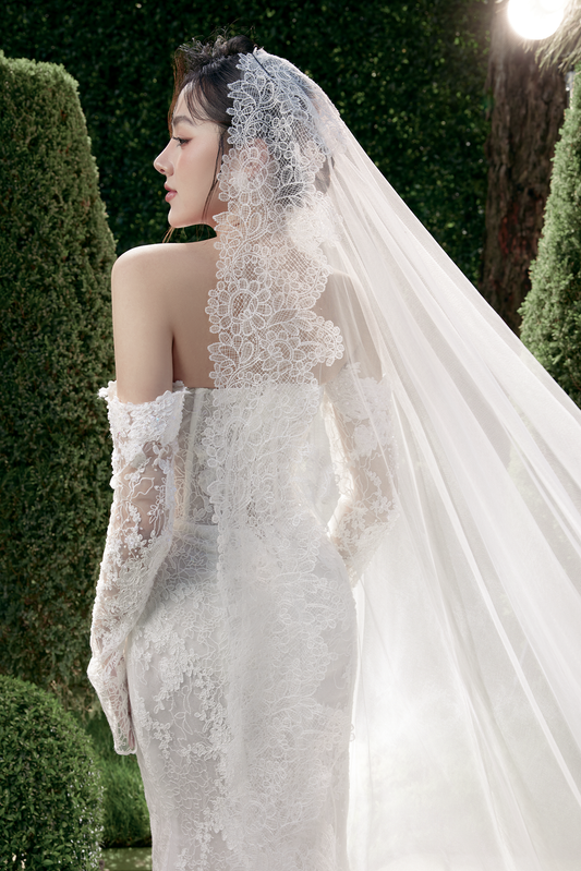 Woman in a white wedding dress with a veil standing outdoors.