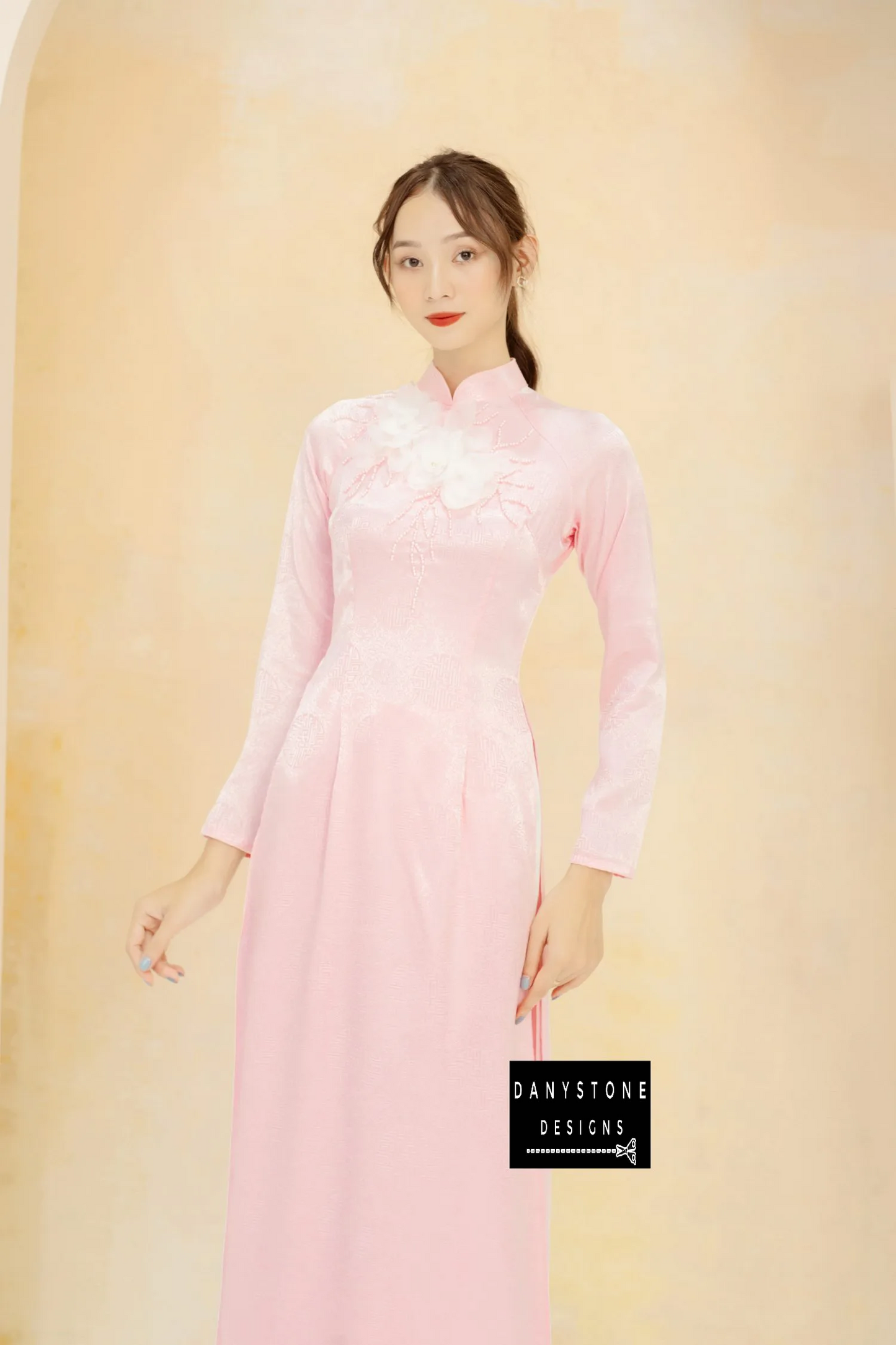 Woman in a pink brocade Áo Dài with four panels, showcasing white floral details.