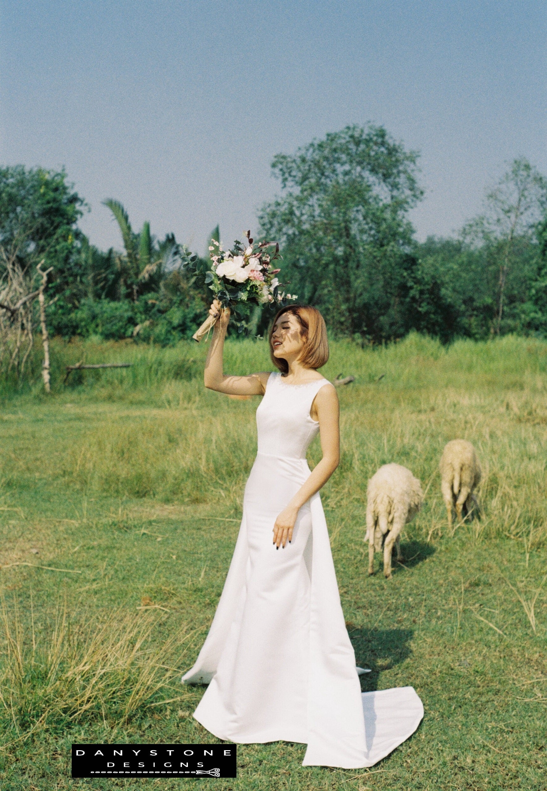 Bride in a V-Back Wedding Dress with Long Fishtail holding bouquet with sheep in the background