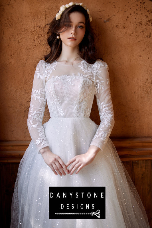 Bride wearing a Cinderella puffy wedding dress with leaf motifs and 3D flowers, standing against an orange wall.