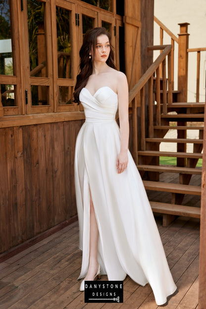 Bride standing on a wooden porch, wearing a pleated strapless wedding dress with loose floral sleeves.