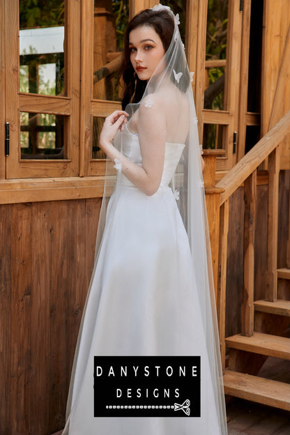 Back view of the bride wearing a pleated strapless wedding dress with a long veil, adorned with flower details.