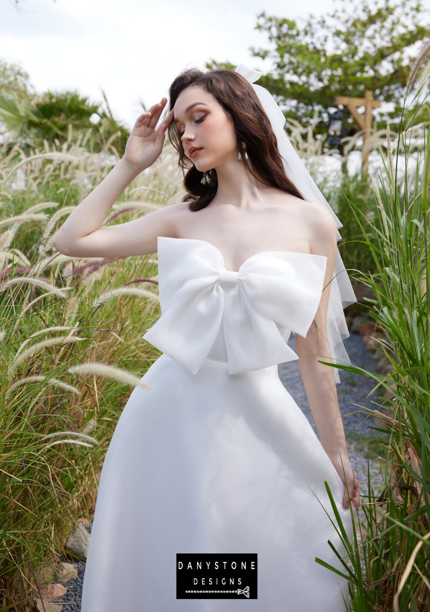 Elegant strapless wedding dress with bow accent by Danystone Designs - front view in a garden setting.