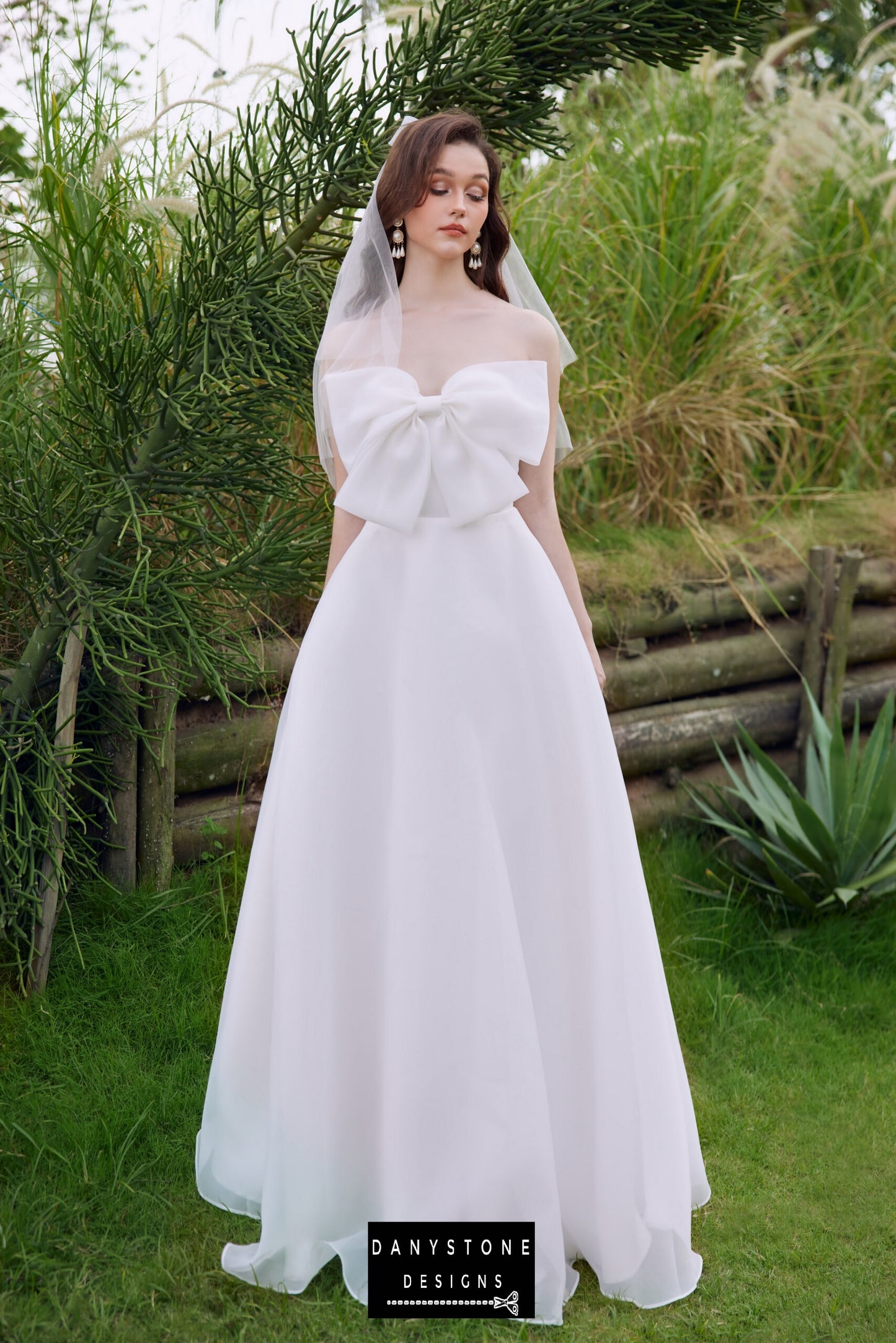 Side view of the strapless bow-accented wedding dress in a natural setting - Danystone Designs.