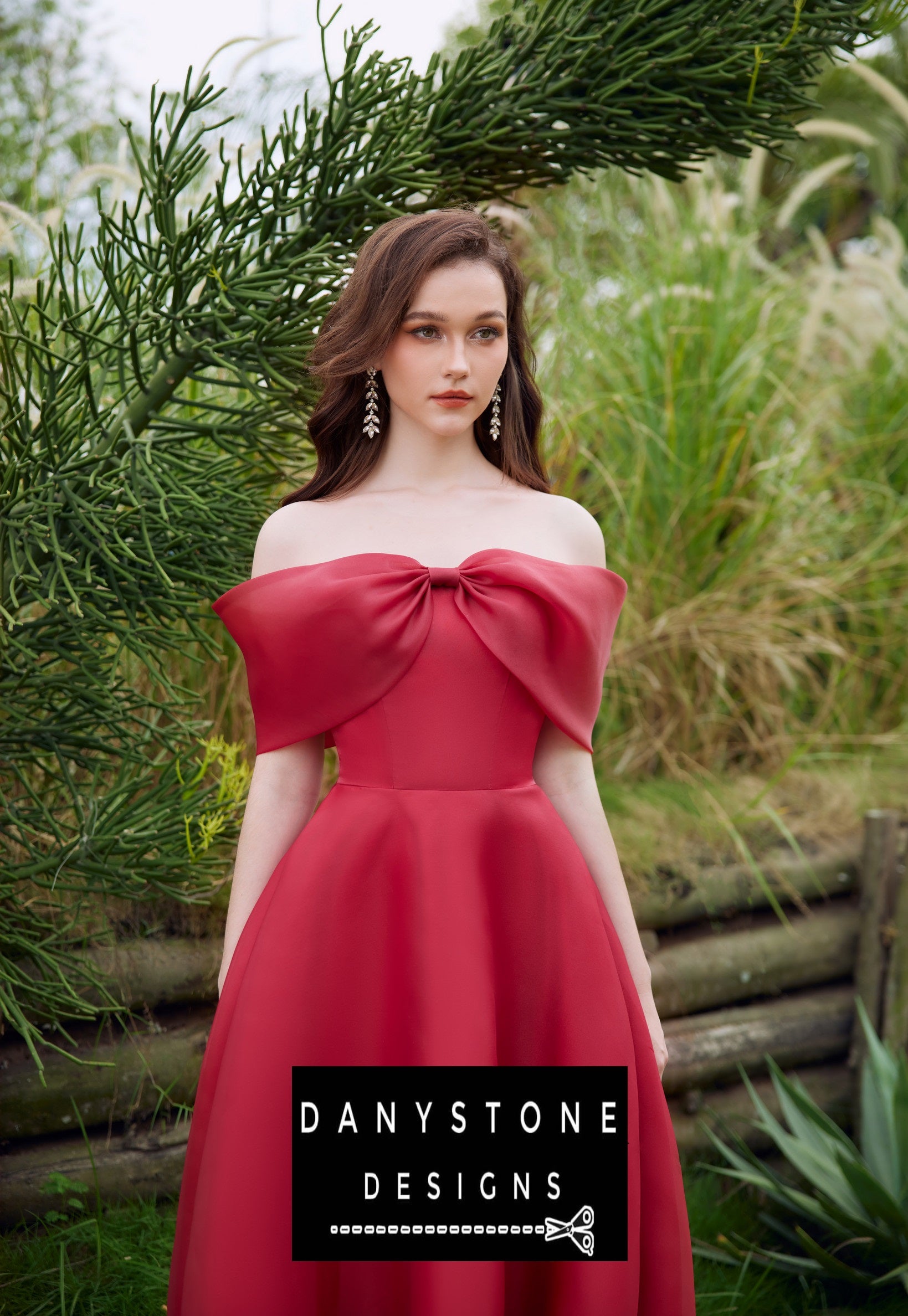 Red off-shoulder silk chiffon dress with chest bow modeled in a garden