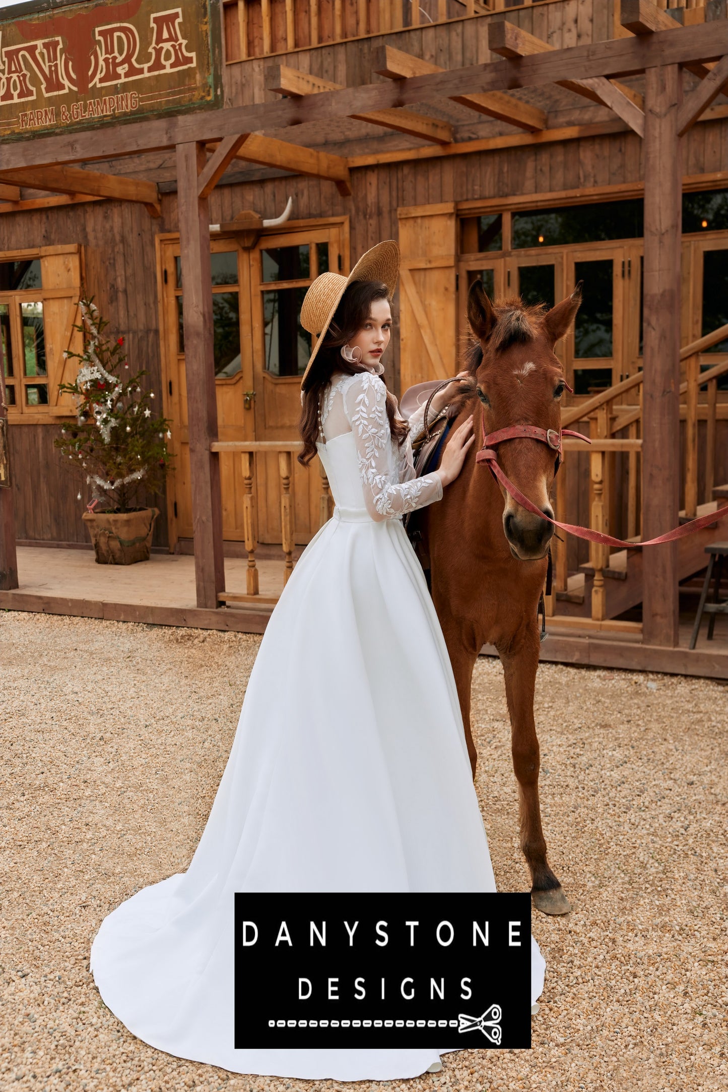 Bride posing with a horse in a long-sleeved fishtail wedding dress with leaf motifs and 3D flowers, with a rustic backdrop.